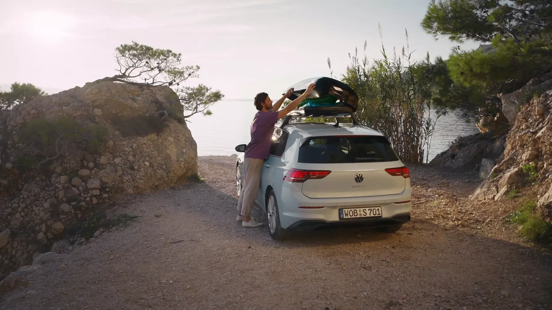 A driver loading a roof box onto a Volkswagen Golf beside the coast
