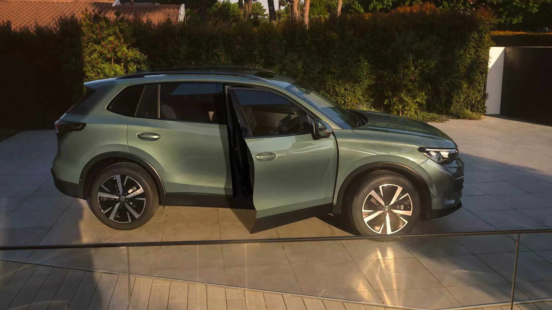 A green Volkswagen Tiguan with its front door open, parked on a paved driveway
