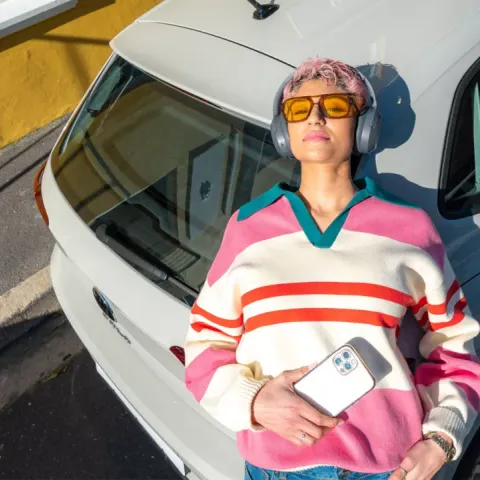 A woman wearing headphones leans against the back of a Volkswagen